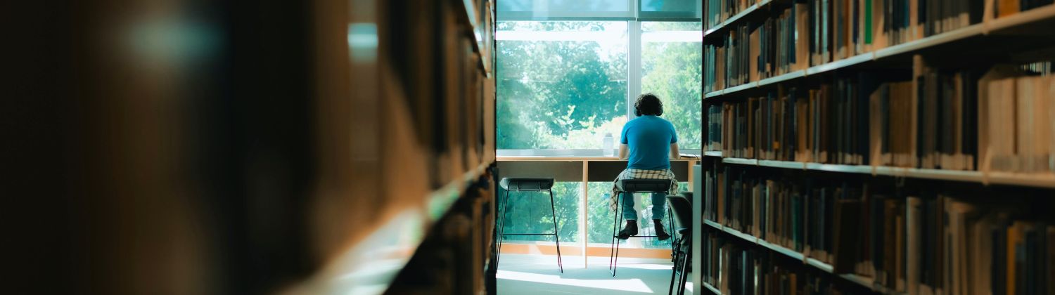 Étudiant travaillant seul dans une bibliothèque universitaire, illustrant les effets du financement des universités sur la recherche et l’accès au savoir au Québec.